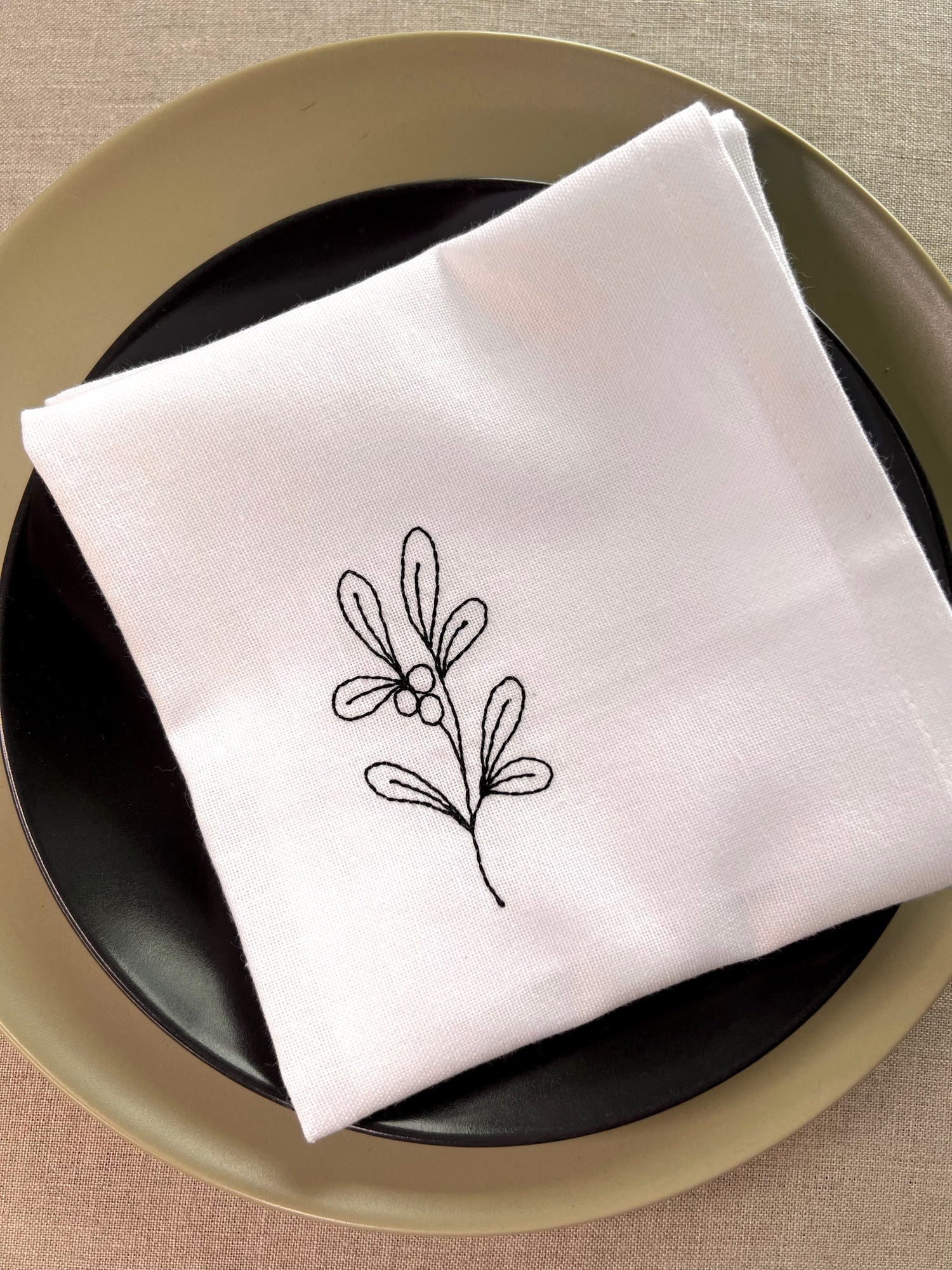 Festive napkin embroidered mistletoe motif in black thread