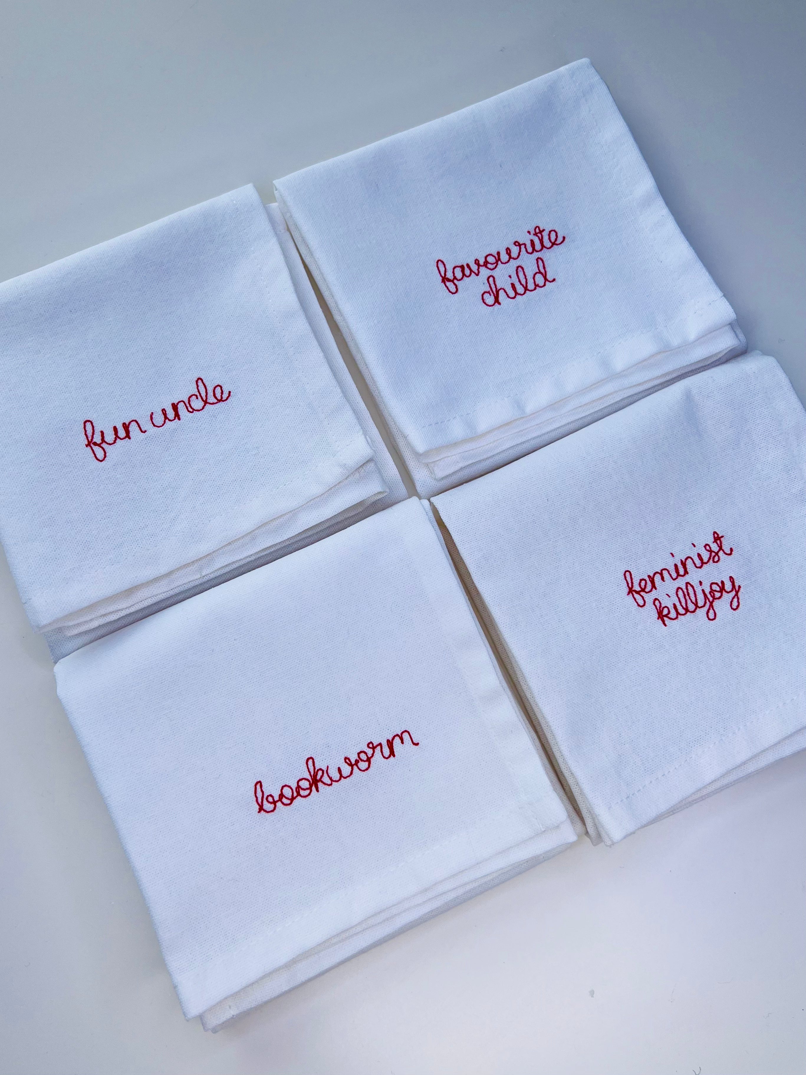 Personalised embroidery on napkins for gifts and table settings with red thread and phrases including bookworm, fun uncle, feminist killjoy, favourite child
