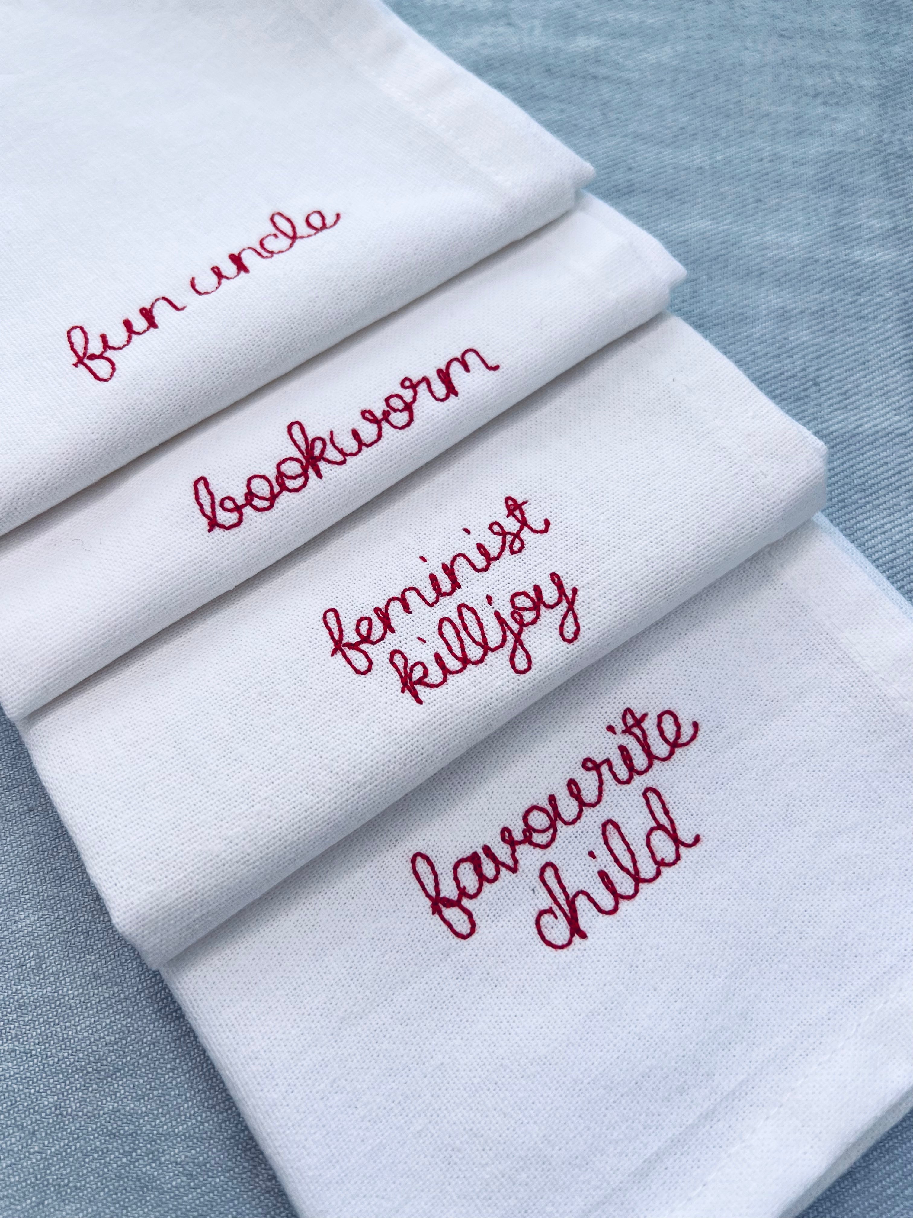 Custom embroidered napkins with family nicknames including favourite child, feminist killjoy, bookworm, fun uncle