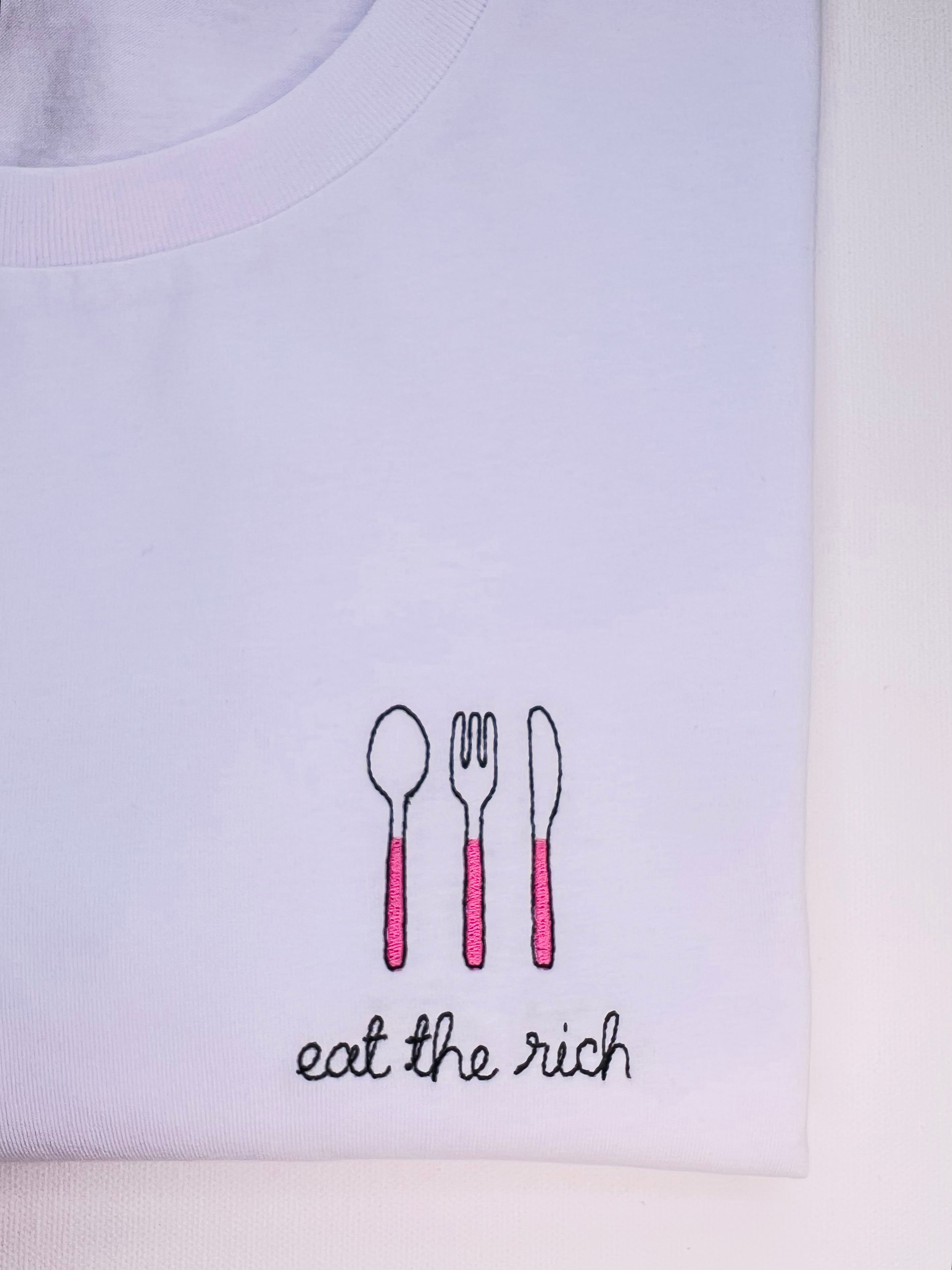 White tshirt with embroidered cutlery motifs and eat the rich text