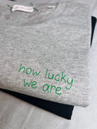 Grey tee with the words ‘how lucky we are’ custom handwriting embroidered in green thread
