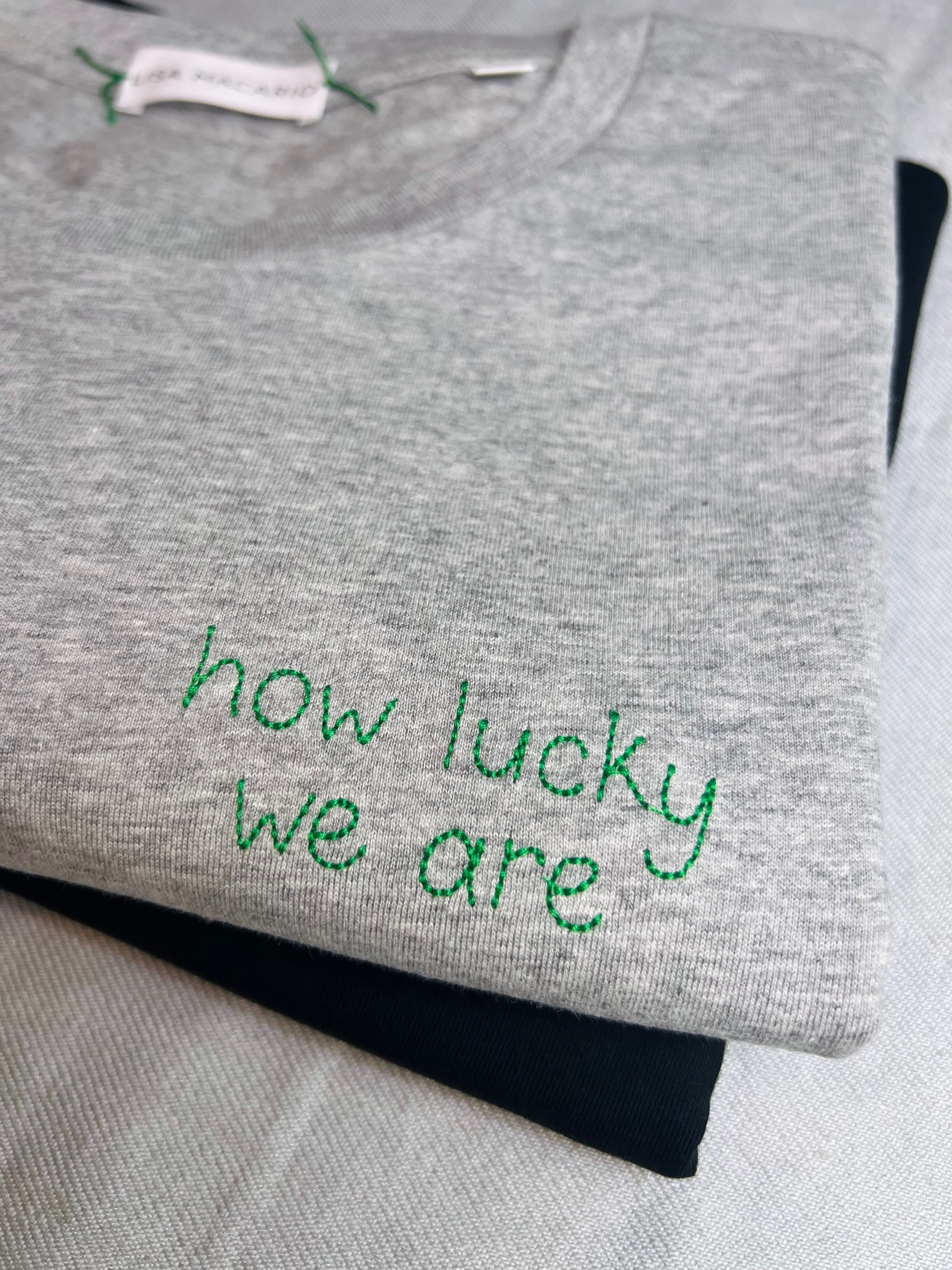 Grey tee with the words ‘how lucky we are’ custom handwriting embroidered in green thread
