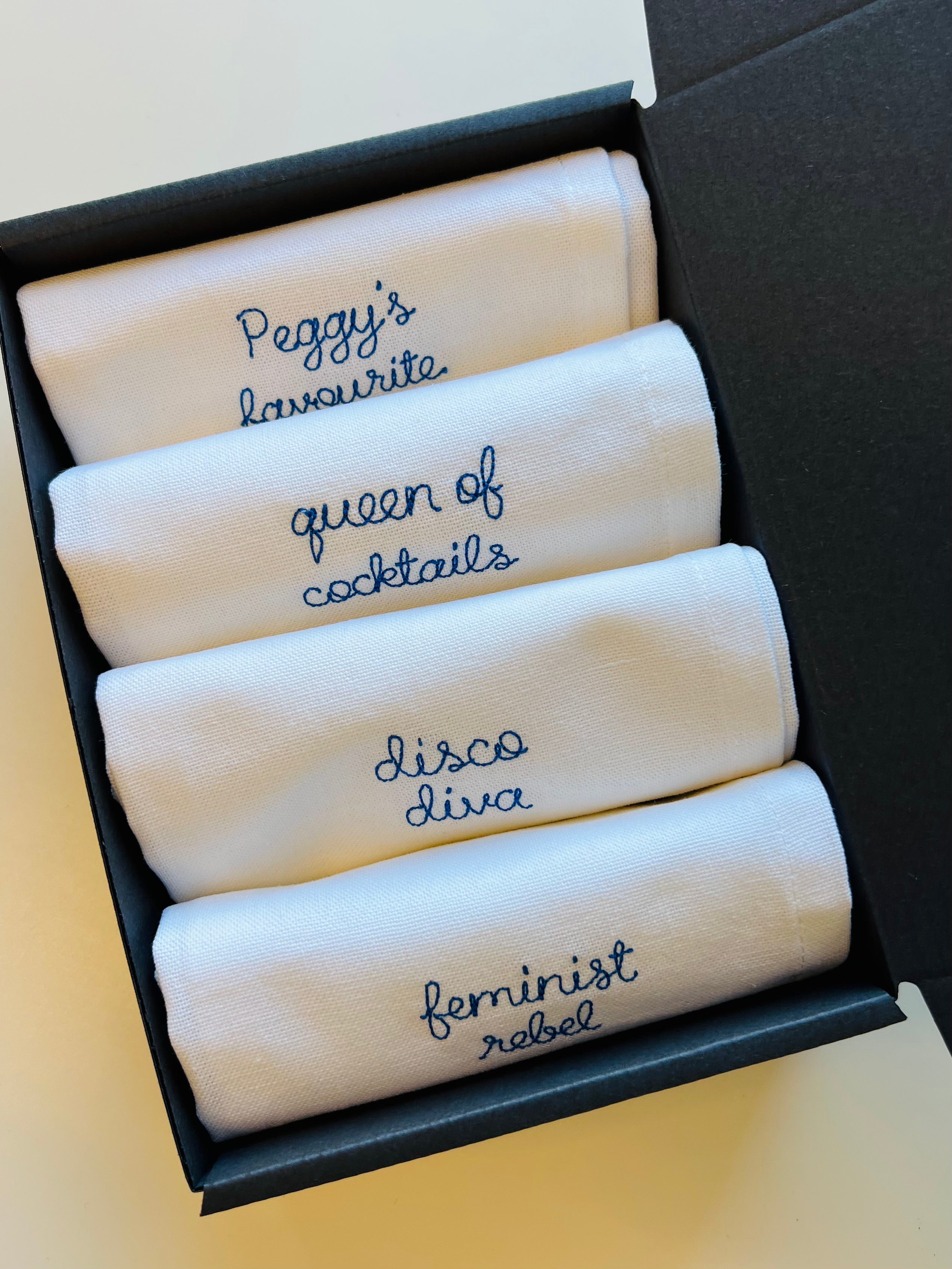 A set of custom embroidered napkins with nicknames including queen of cocktails, feminist rebel and disco diva