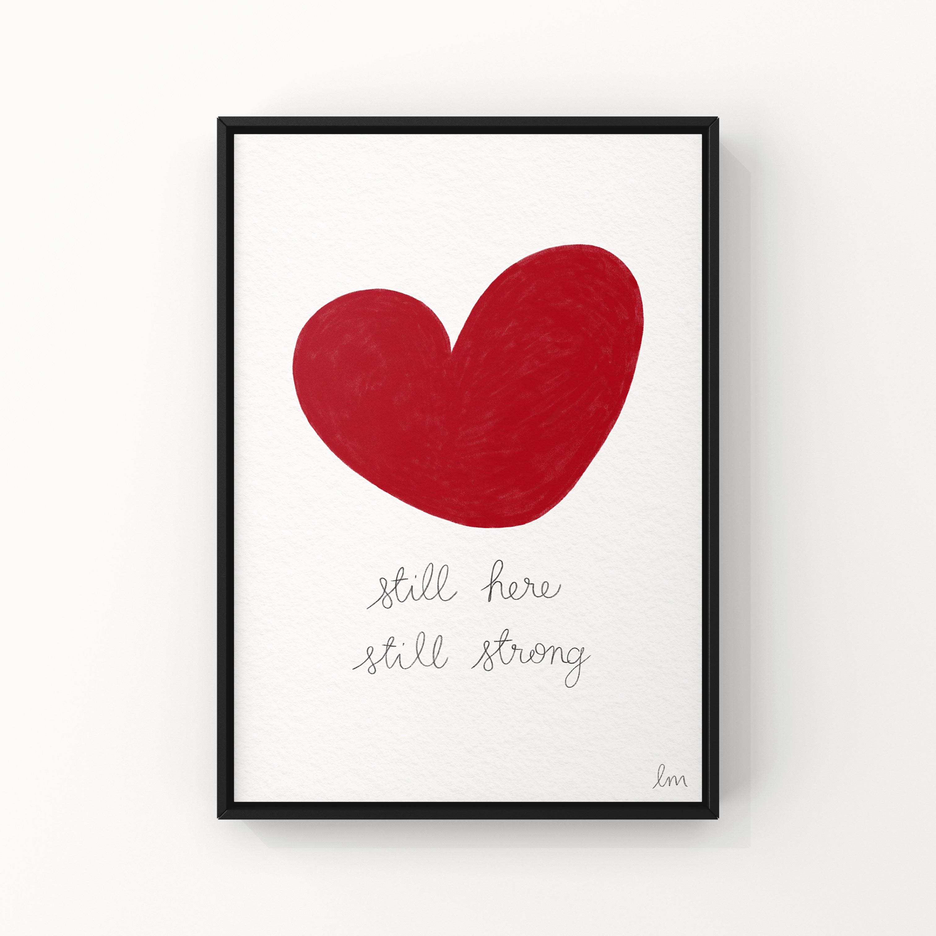 Framed artwork with a red heart and text 'Still here, still strong' on a white background