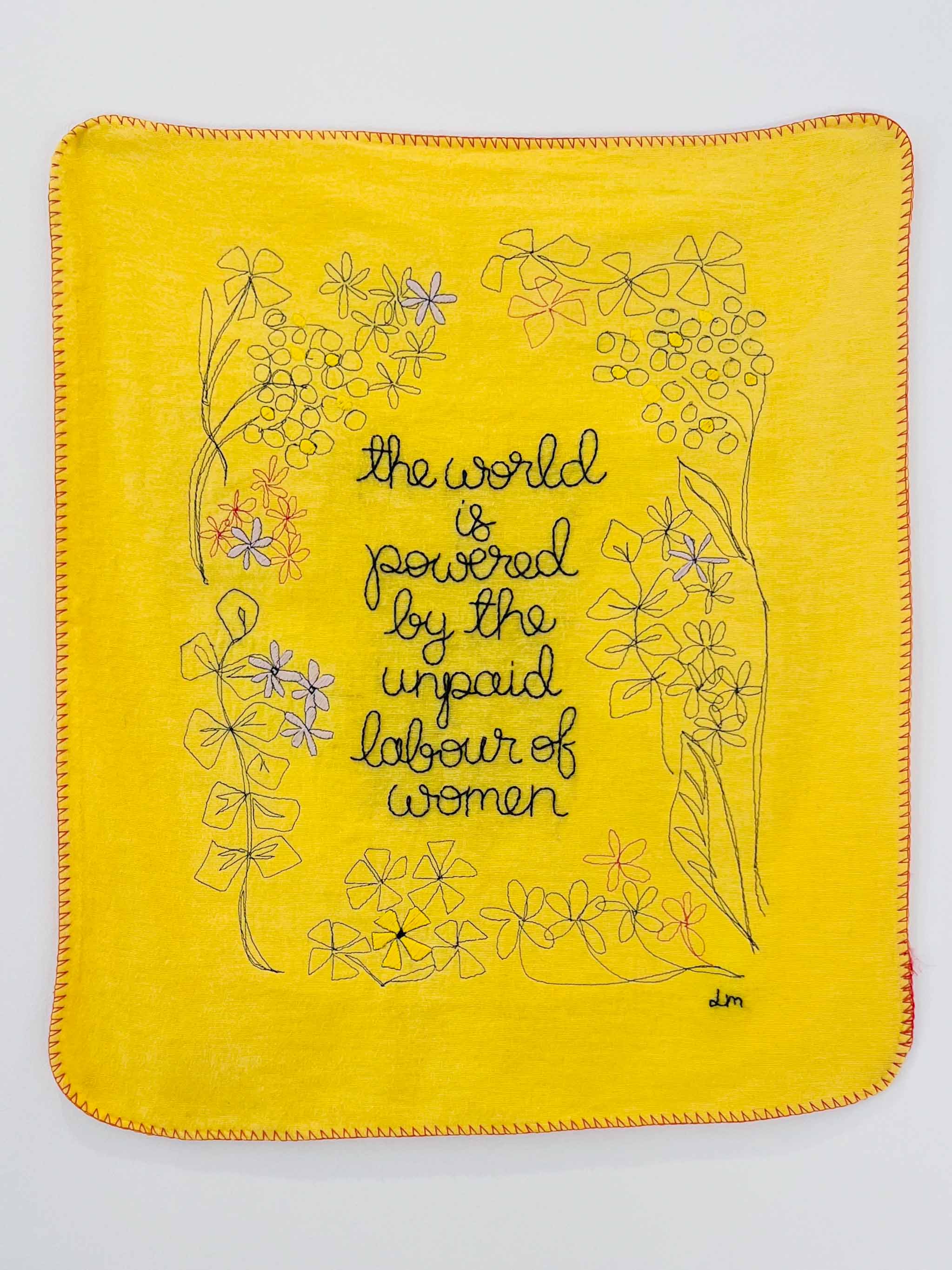 Yellow domestic duster embroidered with ‘the world is powered by the unpaid labour of women’, part of an artwork addressing the unpaid care work performed by women and girls. Displayed in the ‘OBJECTS’ exhibition at Blackwater Gallery, Cardiff, 2022