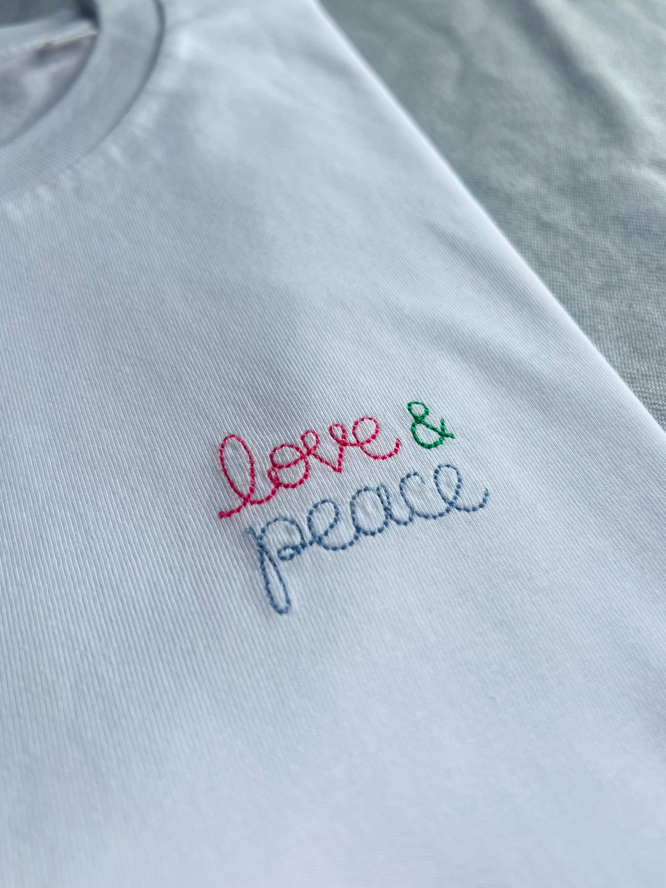white t-shirt with 'love & peace' embroidered in pink, green, blue thread, custom bespoke slogan embroidery