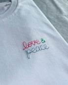 white t-shirt with 'love & peace' embroidered in pink, green, blue thread, custom bespoke slogan embroidery