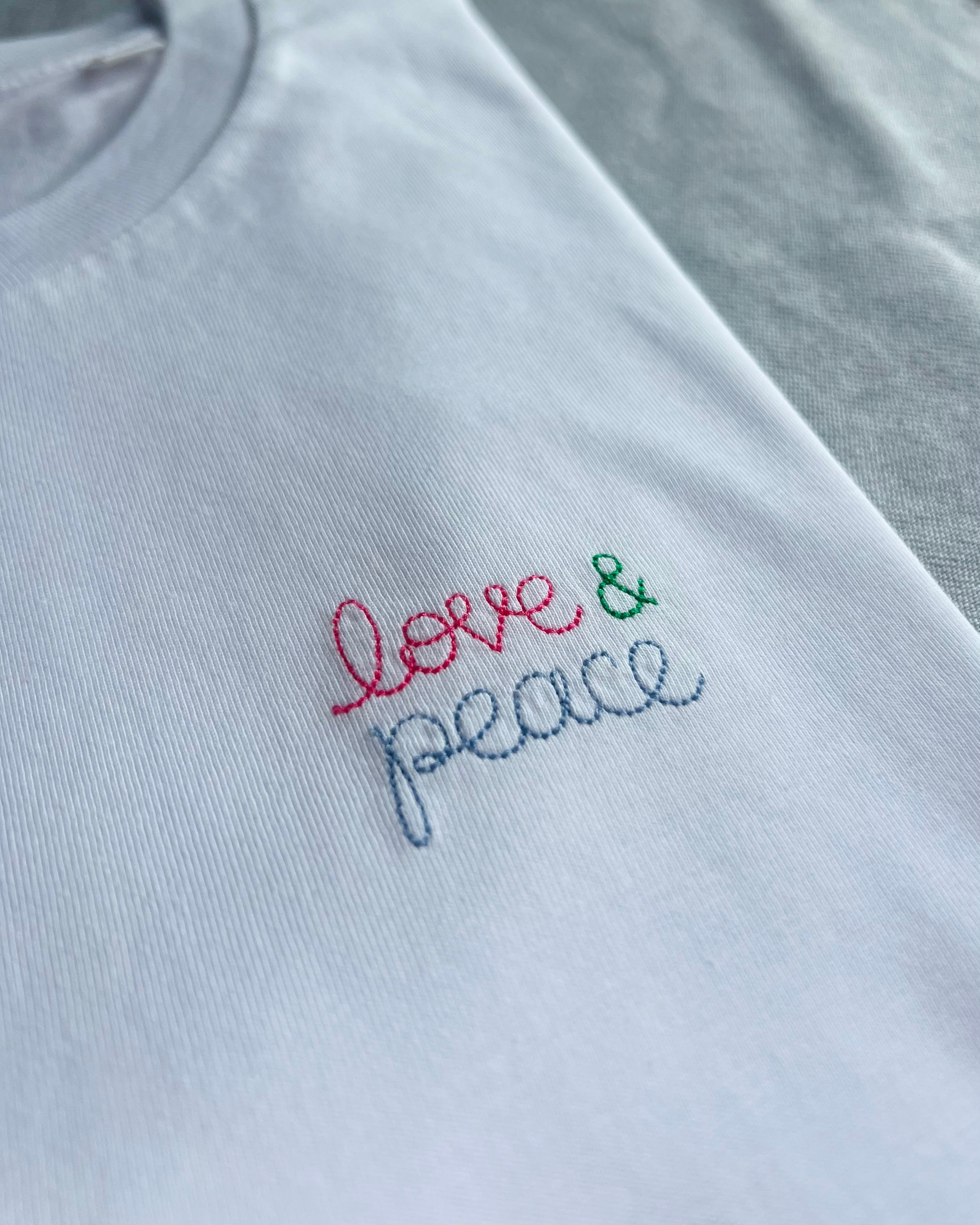 white t-shirt with 'love & peace' embroidered in pink, green, blue thread, custom bespoke slogan embroidery
