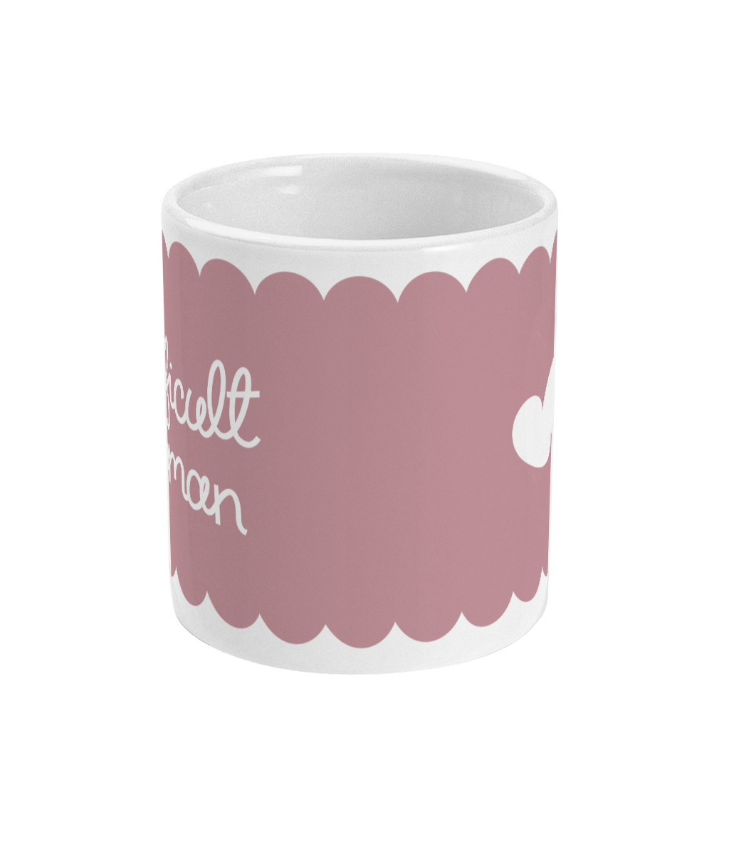 A “difficult woman” ceramic mug with a soft pink background and a scalloped border. The design wraps around, with text on one side and a heart icon on the other.