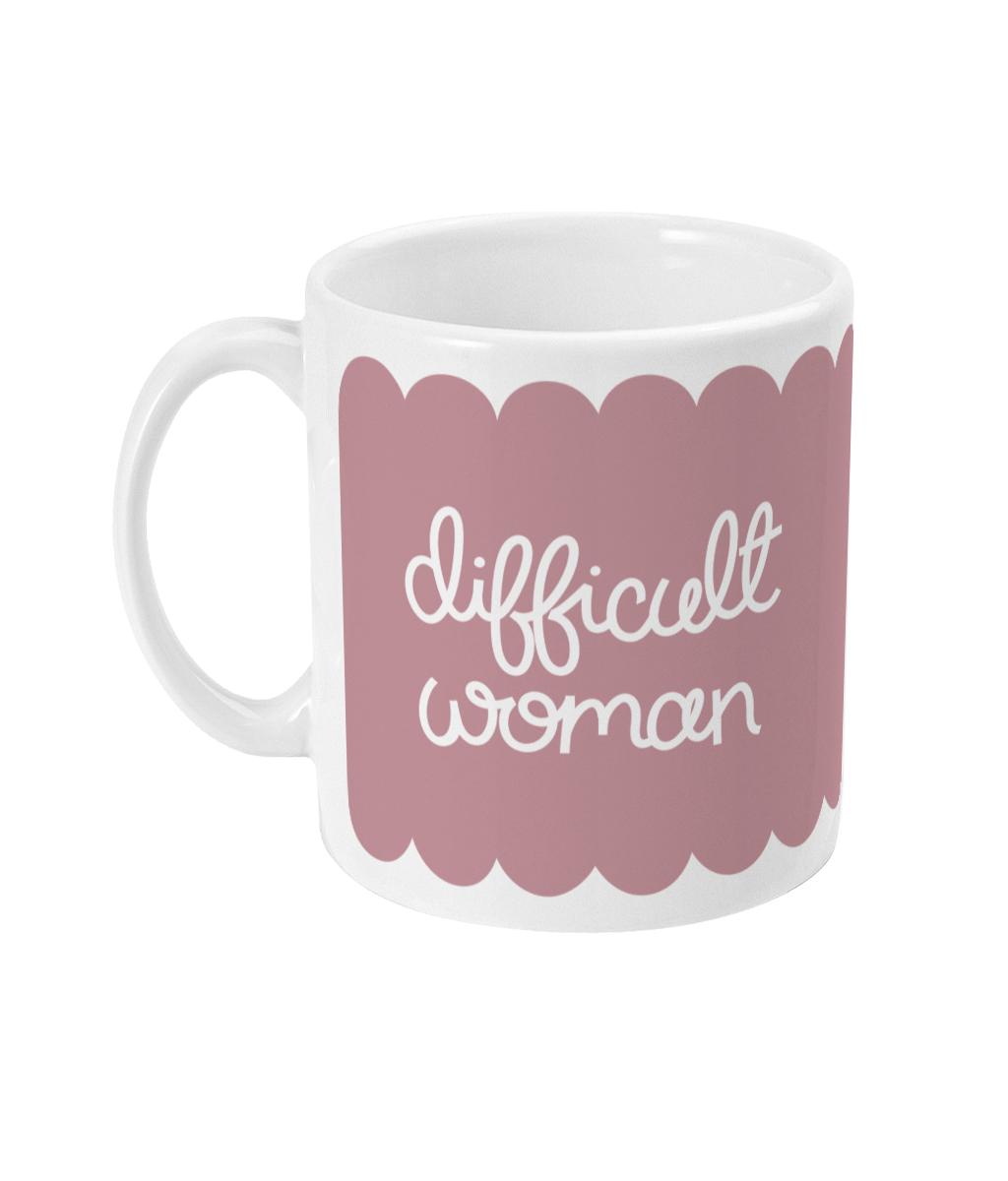 A ceramic mug with a soft pink background and a scalloped border, featuring the phrase “Difficult Woman” in hand-drawn white script.