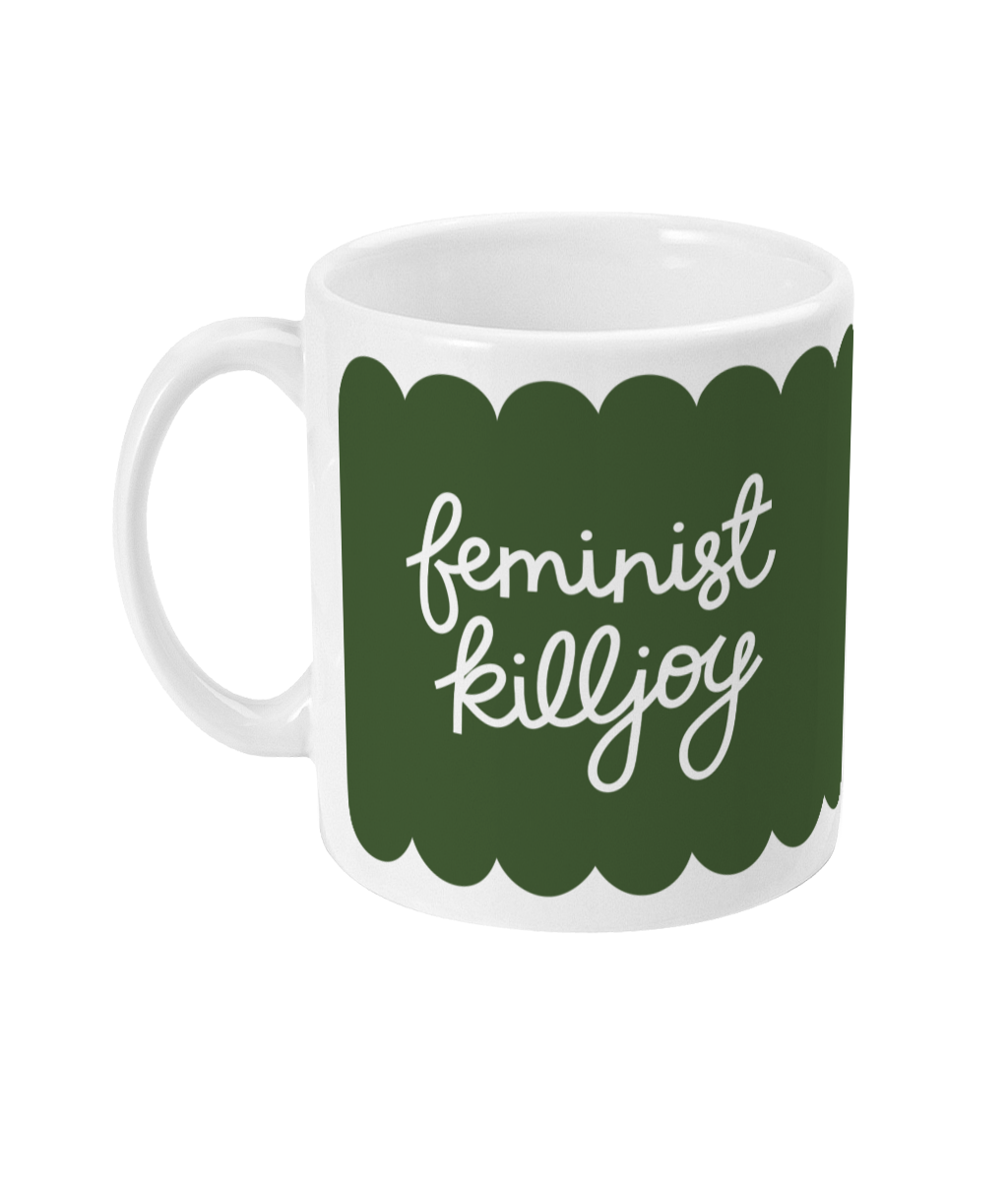 White ceramic mug with an olive green scalloped design, featuring the hand-lettered phrase ‘feminist killjoy’ in white cursive. A small white heart is on the reverse side