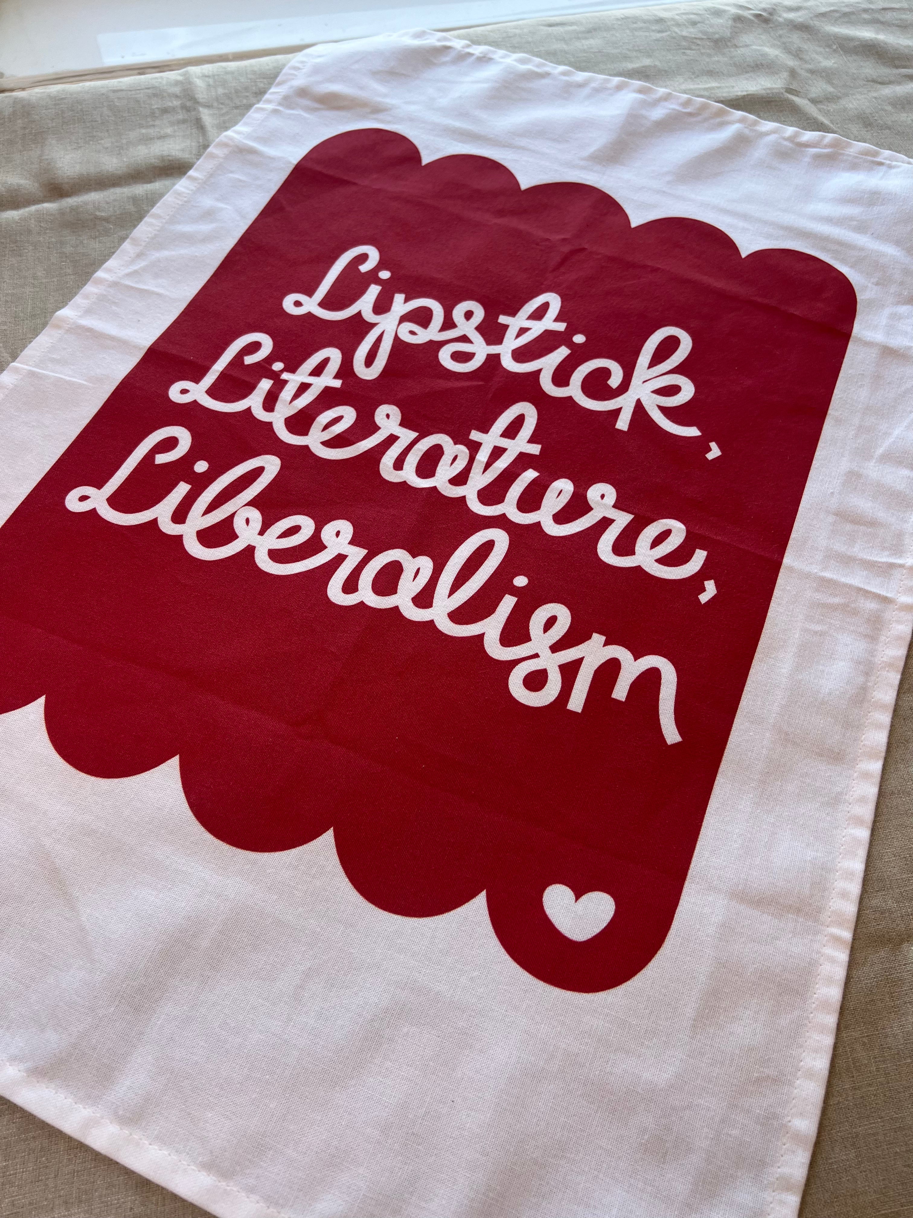 Cotton tea towel with red scallop design and the text lipstick, literature, liberalism 