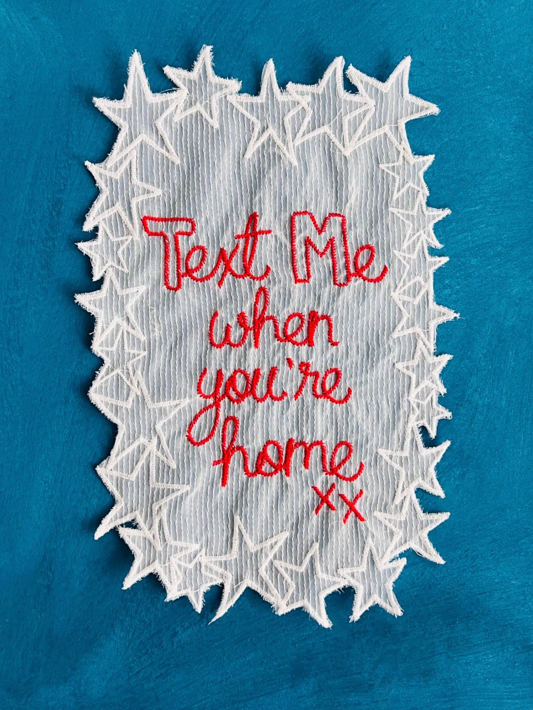 Embroidered artwork with 'Text Me when you're home xx' on a blue background
